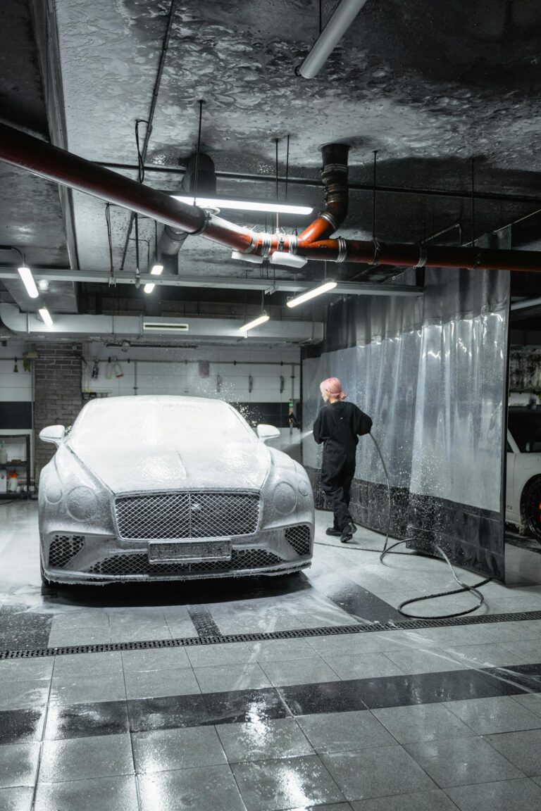 A person washes a luxury car indoors using a pressure washer. Modern automotive care scene.